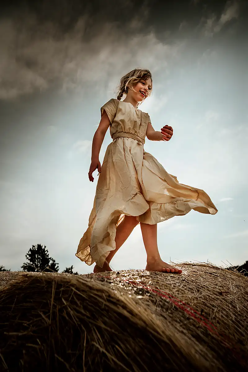 Kind mit Boho Style beim Fotoshooting auf einem Heuballen auf dem Feld