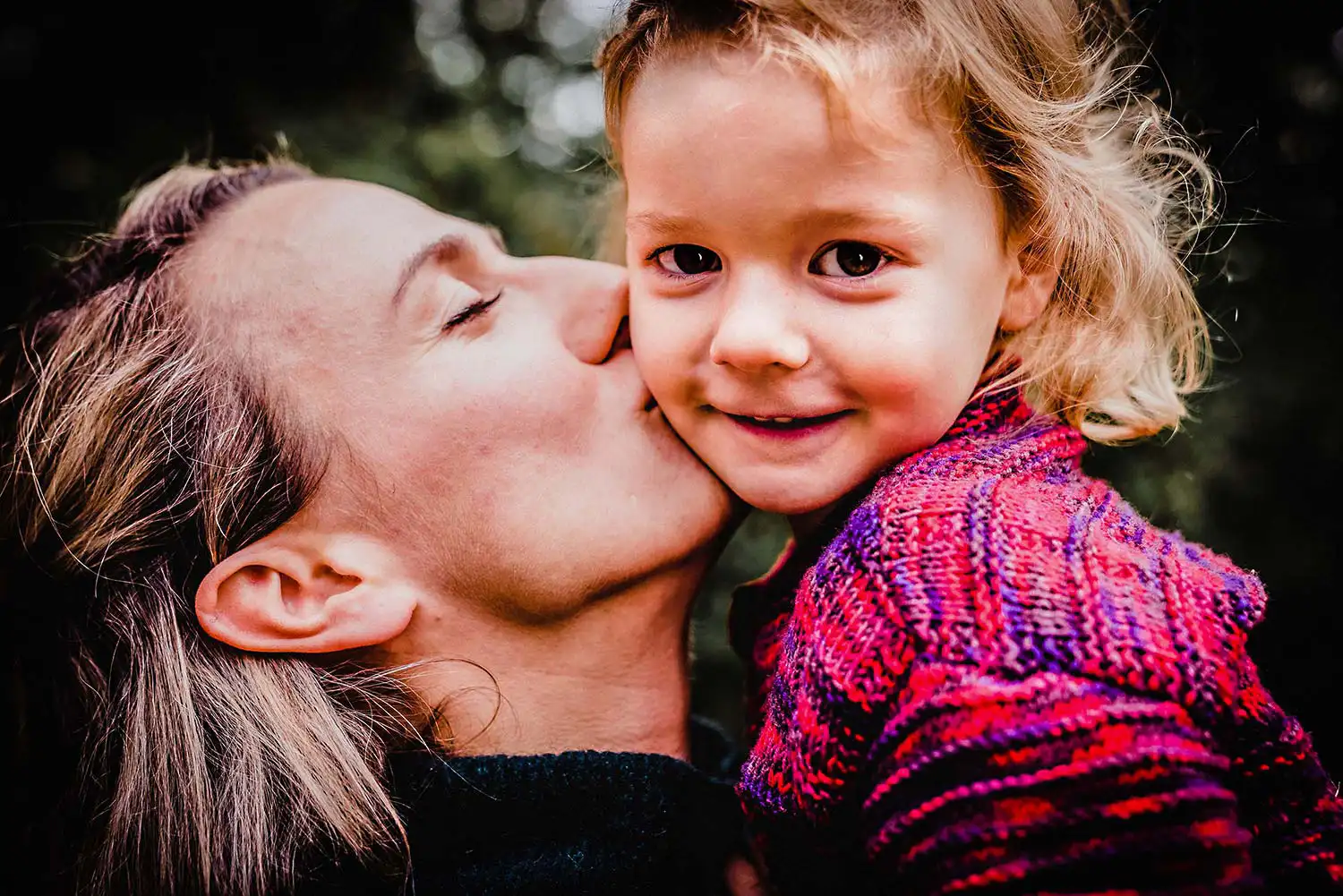 Mutter küsst ihr lächendes Kind beim Familienfoto